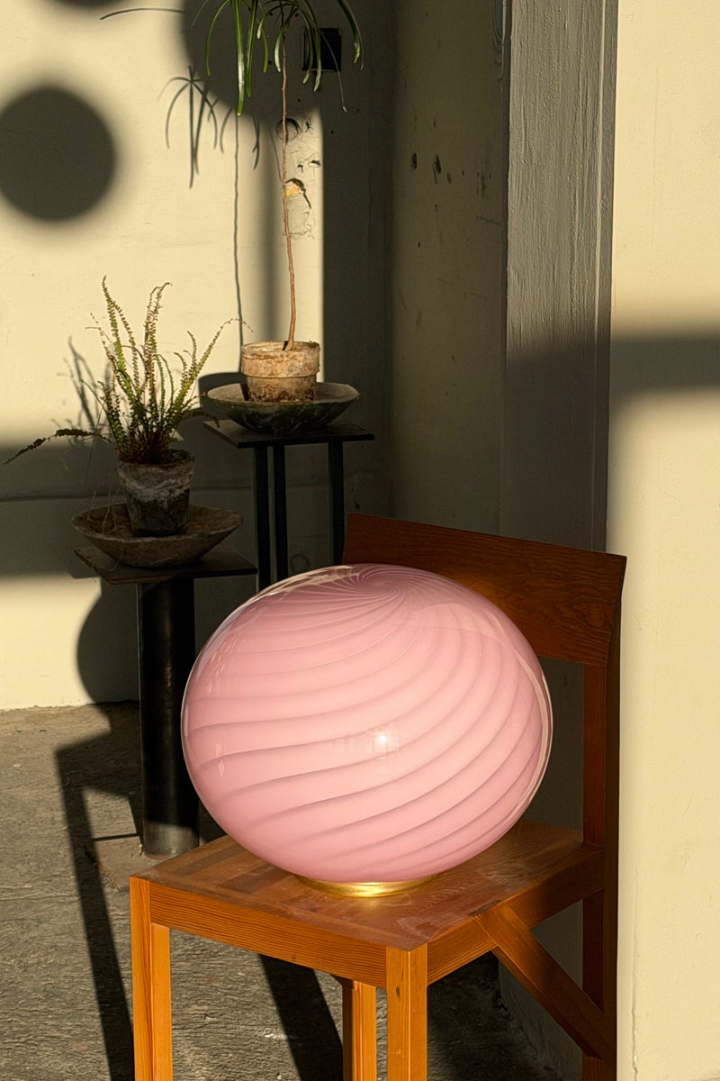 oval Murano gulvlampe i farven bubble gum, set fra siden med swirl mønster, står på en stol i et lyst rum
