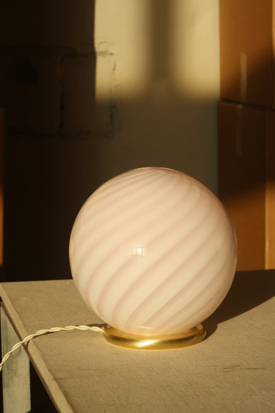 Murano table lamp in soft pink with swirl pattern, seen from the side on a simple surface