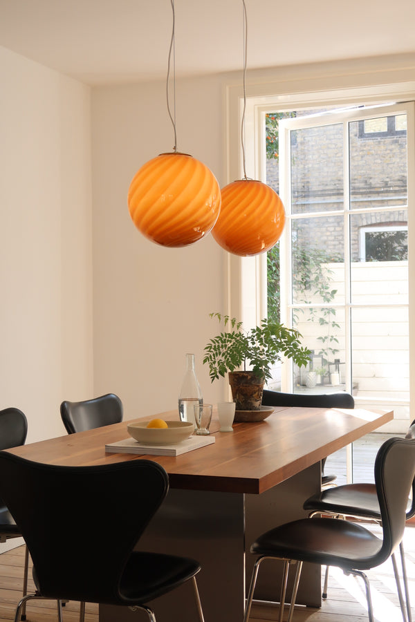 Murano pendel i orange/rav med swirl mønster hængende over spisebord i lyst rum