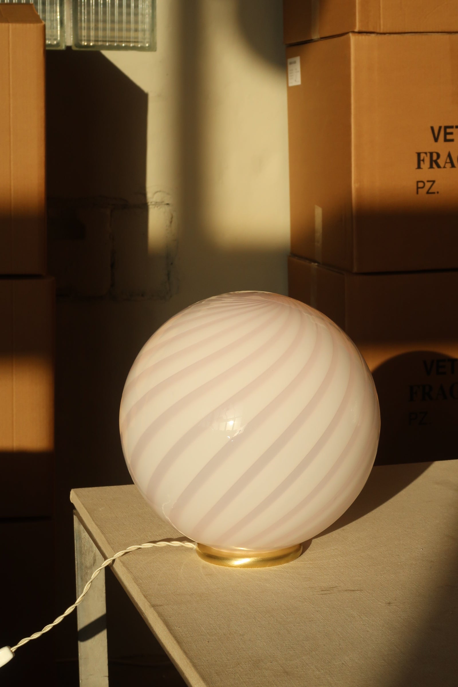 Murano tafellamp in zacht roze met swirl-patroon, gezien vanuit een hoek die schaduwen en lichtreflecties benadrukt