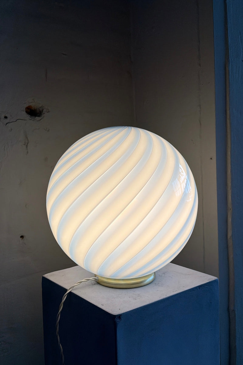 Murano bordlampe med blå swirl mønster, rund form og blødt lys, står på en blå sokkel