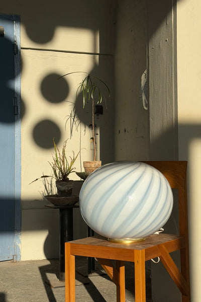 Murano candy oval gulvlampe i lyseblå med swirl mønster, placeret på en træstol i et lyst rum