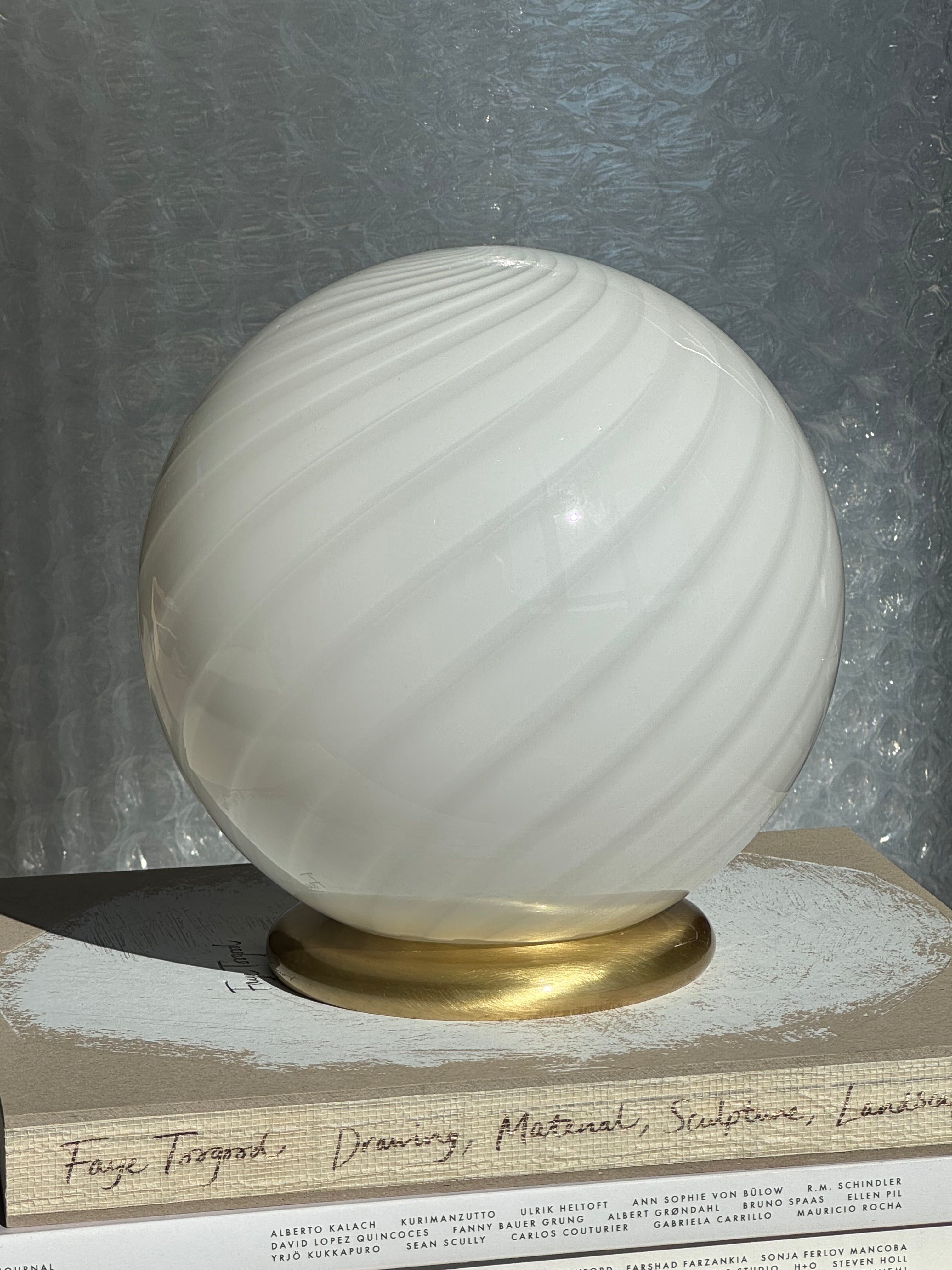 Ny Murano Candy bordlampe med hvid swirl. Mundblæst glas i rund form. E27 fatning samt base med overflade i børstet messing.

Den perfekte størrelse til dit natbord, indbygget reol eller vindueskarm.

Håndlavet i Italien.
D:20 cm
Vægt ca. 1 kg.
