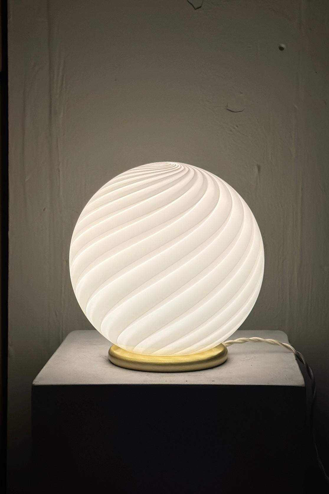 lampe de table rose pâle à motif swirl, vue de côté sur une surface blanche, design élégant et lumineux. Murano