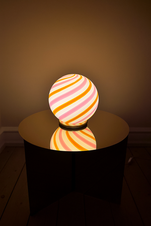 Murano Tischlampe mit gelb/hellrosa Swirl-Muster, auf einem Spiegelbord in sanftem Licht beleuchtet