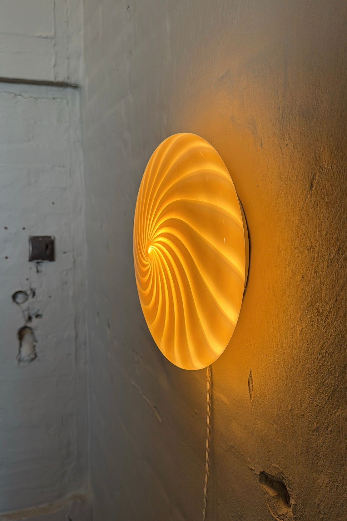 a unique perspective of the Murano ceiling lamp in caramel and cream with a swirl pattern, beautifully lit against the wall