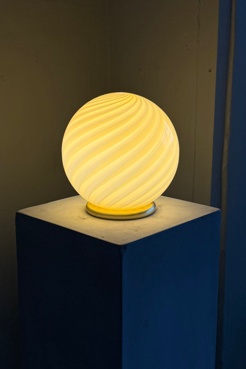 Murano bordlampe i gul med swirl mønster, smukt belyst fra siden på hvid sokkel