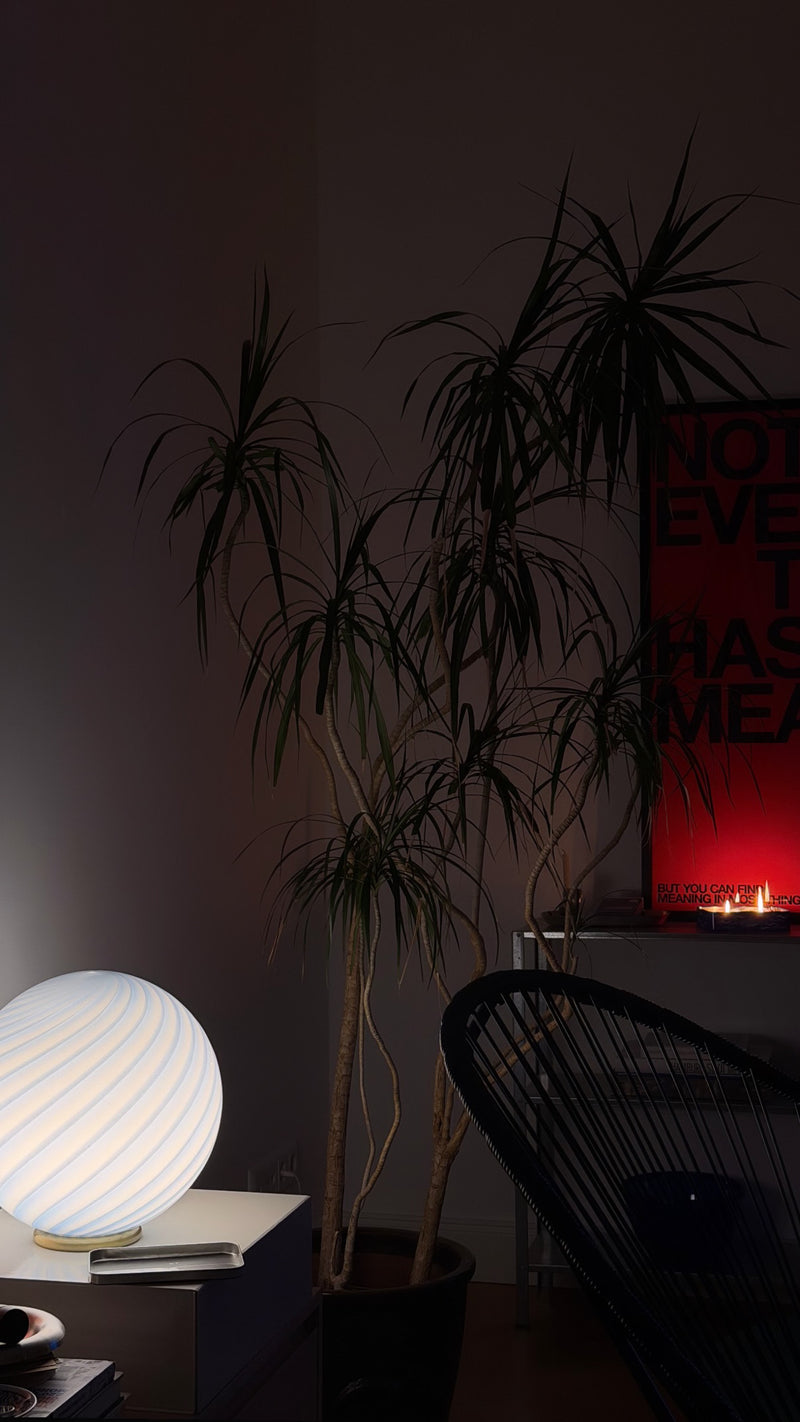Murano bordlampe med blå swirl mønster, elegant placeret ved en plante i et moderne rum