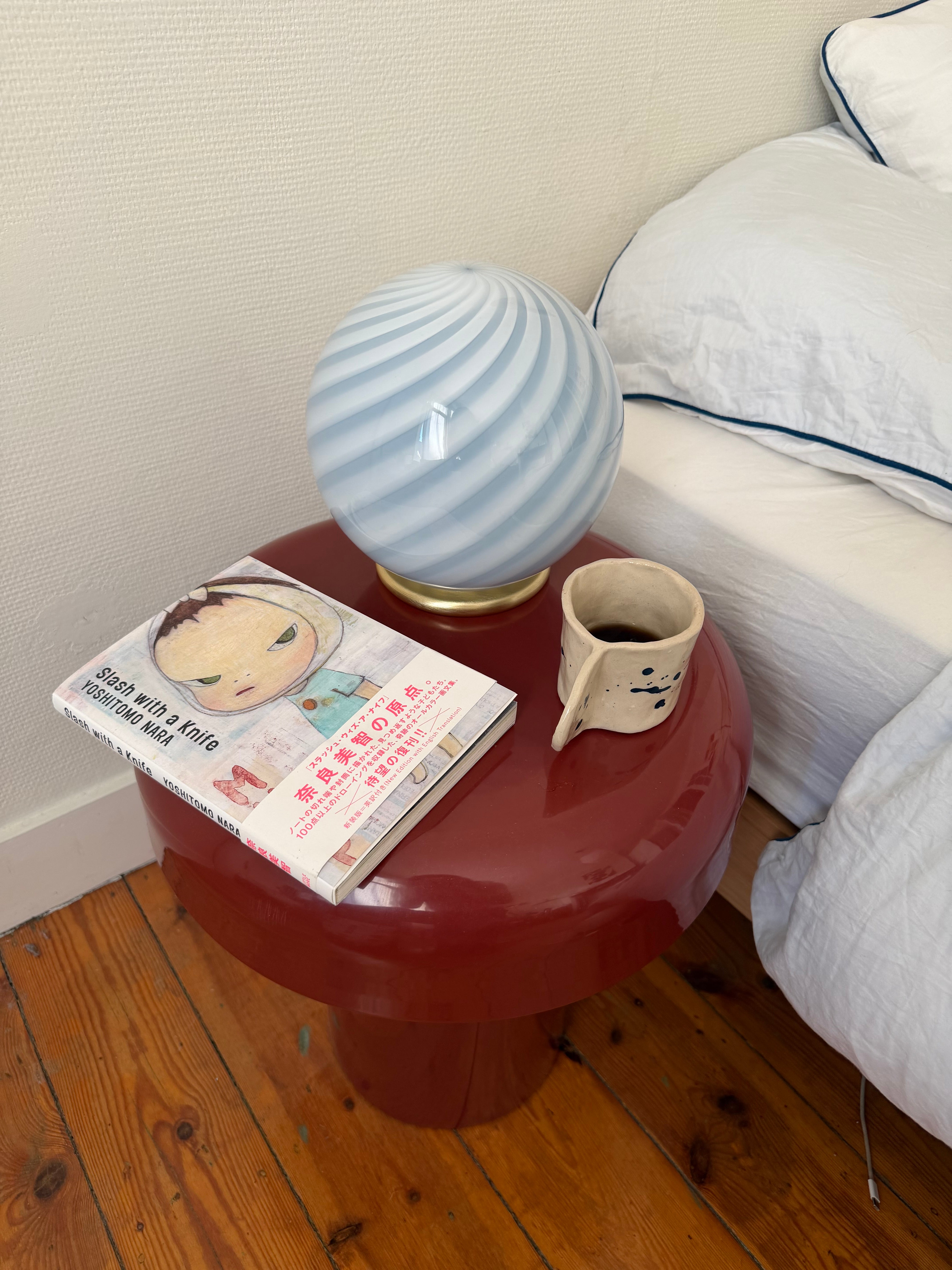 murano table lamp in light blue with swirl pattern, placed on a red side table by a bed