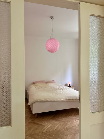 large Murano pendant in bubble gum color with swirl pattern hanging over the bed in a bright room