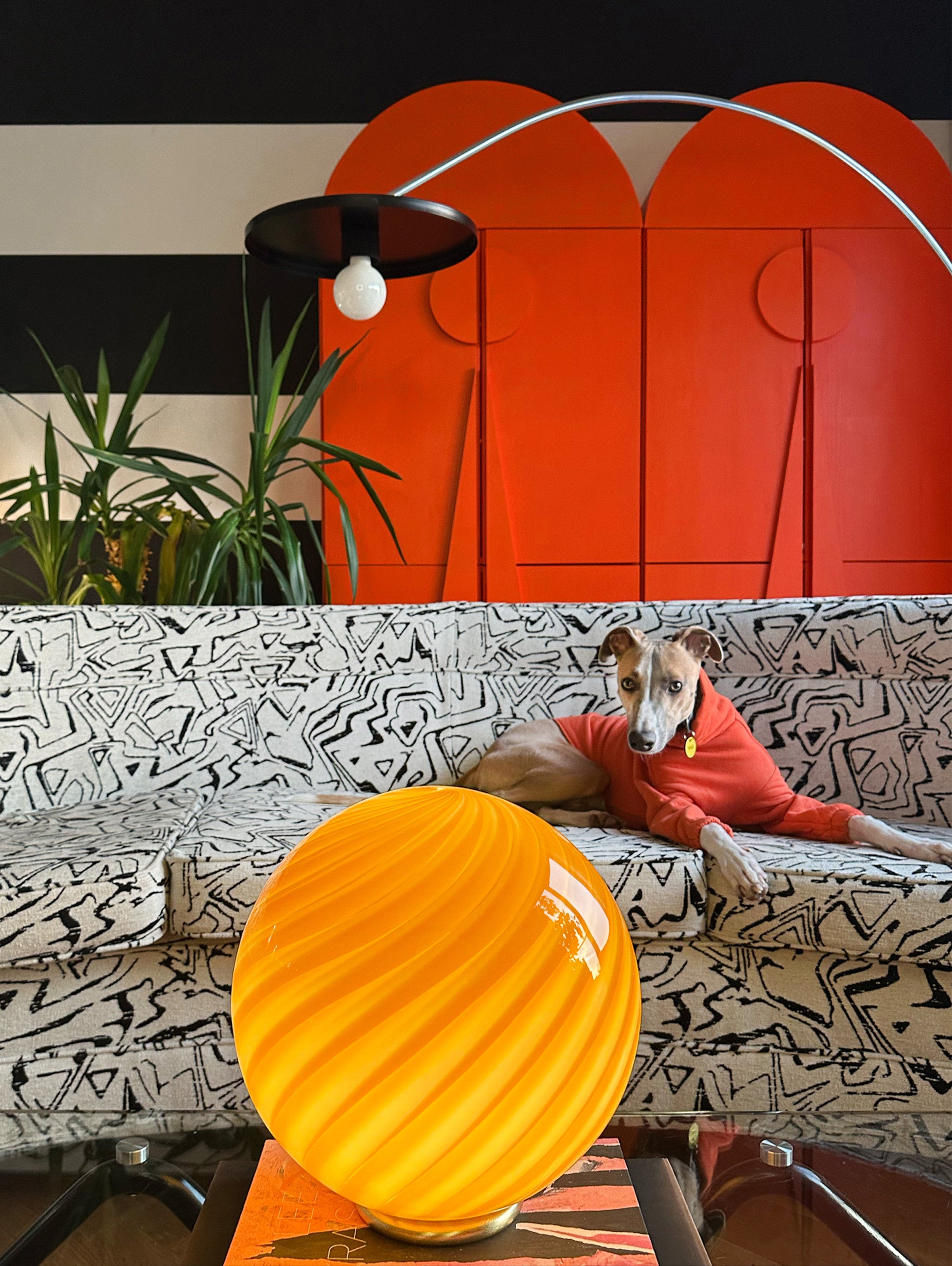 Murano bordlampe i rav orange med swirl mønster, præsenteret i en moderne stue med sofa og planter
